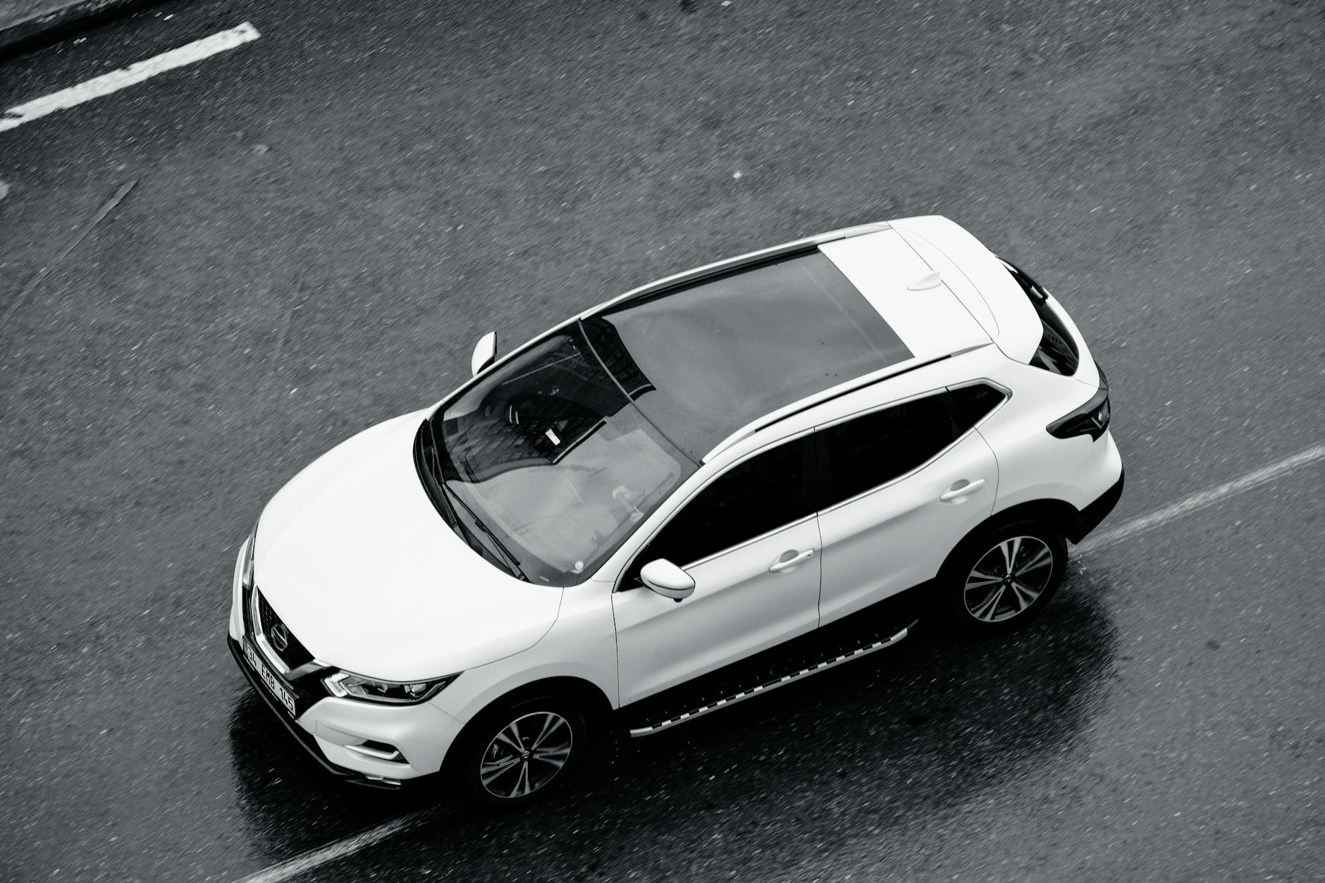 Białe SUV jedzie po mokrej ulicy dużego miasta z lotu ptaka