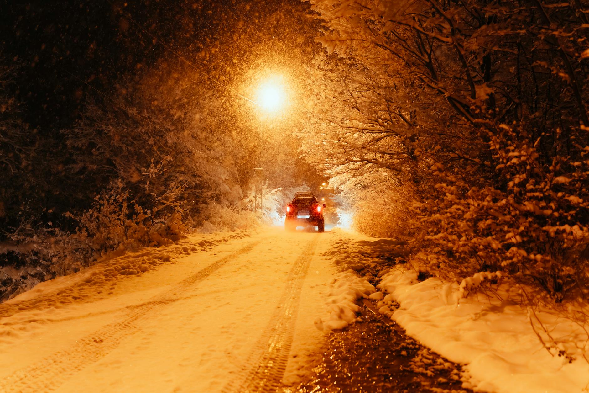 Samochód jedzie ośnieżoną ulicą nocą w świetle latarni