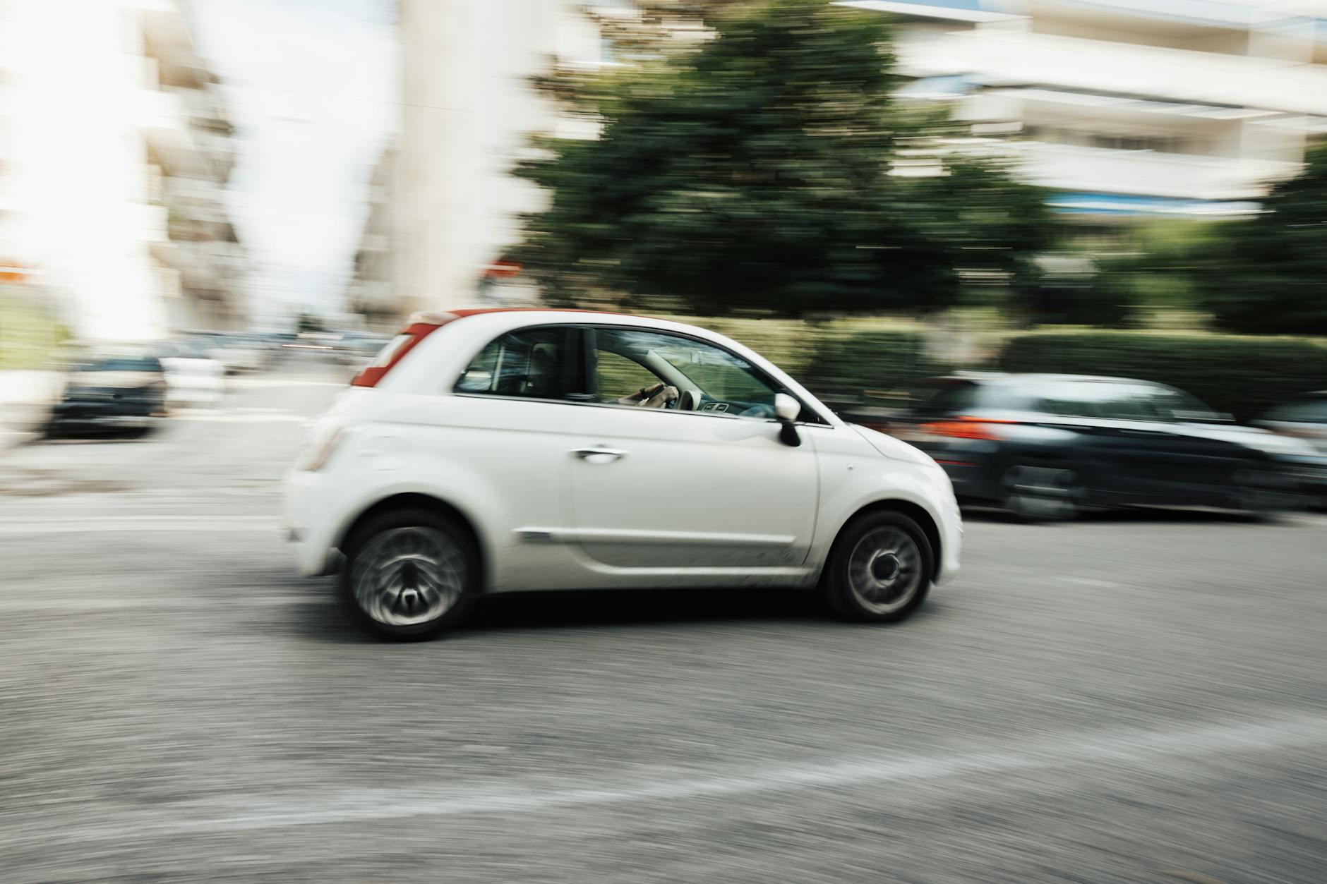 Białe auto jedzie szybko po miejskiej ulicy, rozmazane tło miasta