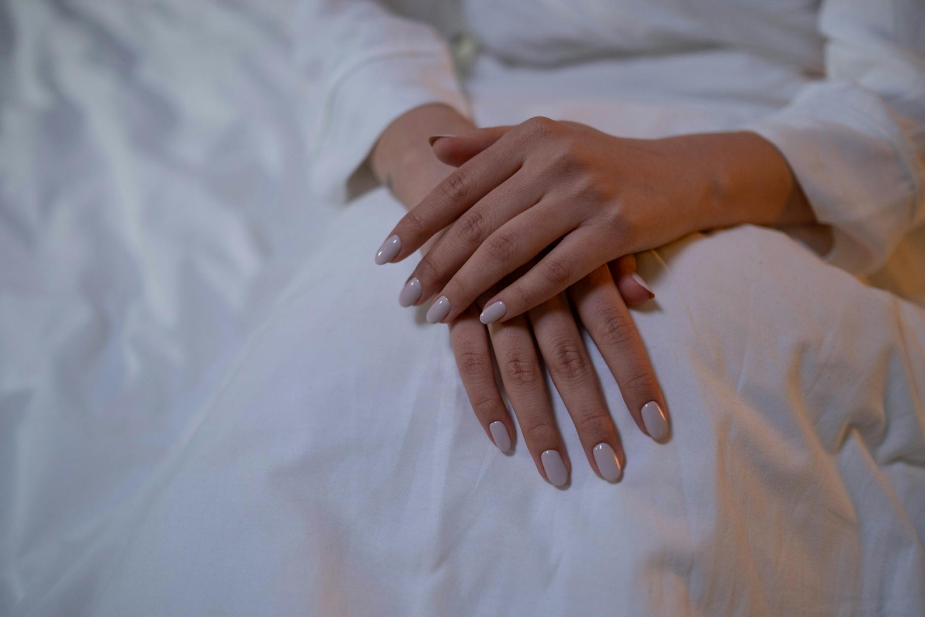 Dłonie z minimalistycznym, nude manicure hybrydowym na białej tkaninie