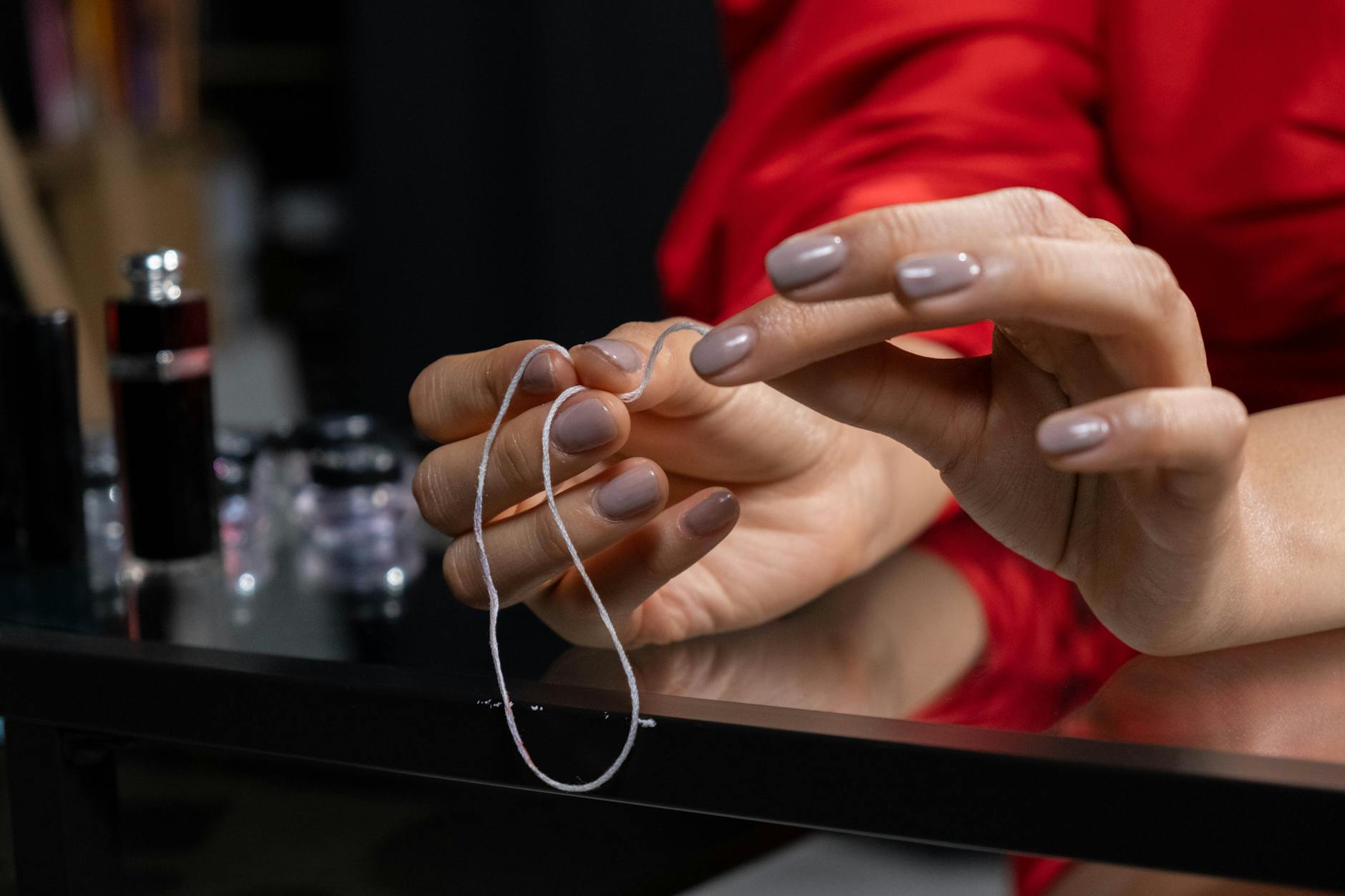 Zbliżenie dłoni z minimalistycznym manicure hybrydowym oplatających nić