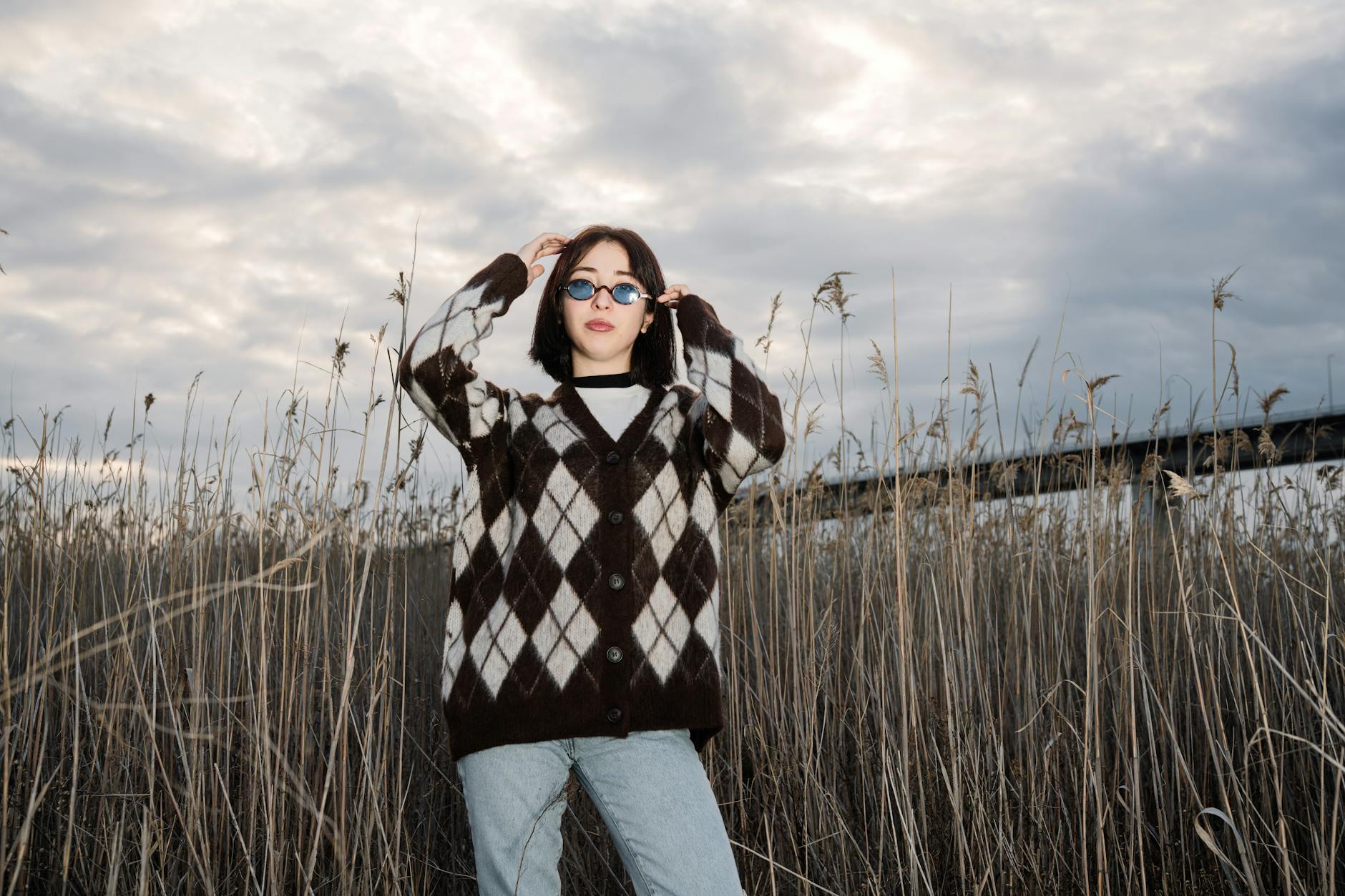 Kobieta w oversize swetrze argyle i okularach przeciwsłonecznych wśród traw