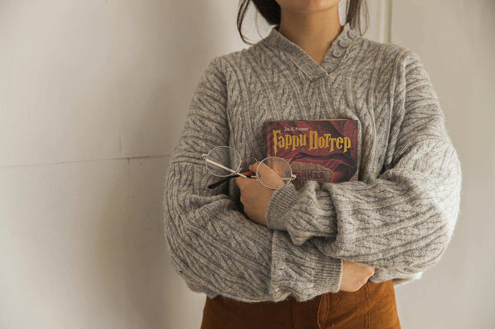 Kobieta w oversize swetrze trzyma książkę i okulary w jesiennym wnętrzu