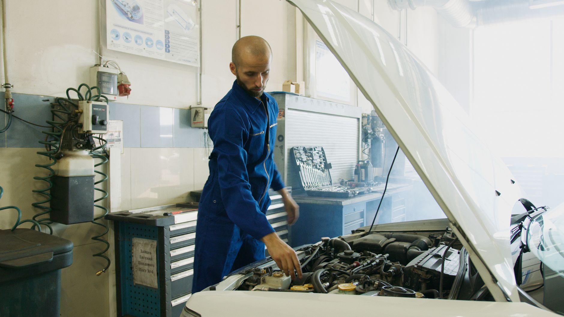 Mechanik w niebieskim uniformie sprawdza silnik Maserati w warsztacie Mechanik w niebieskim uniformie sprawdza silnik Maserati w warsztacie