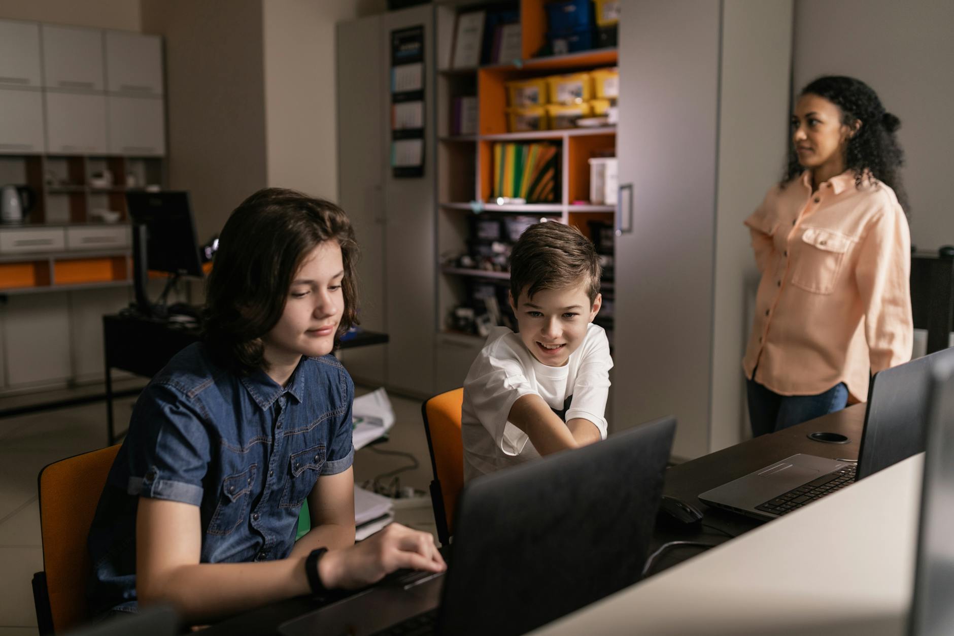 Nauczyciel nadzoruje uczniów pracujących na laptopach w klasie