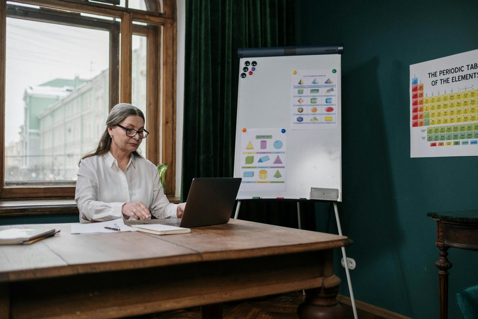 Starsza kobieta w klasie pracuje na laptopie z tablicą chemiczną w tle