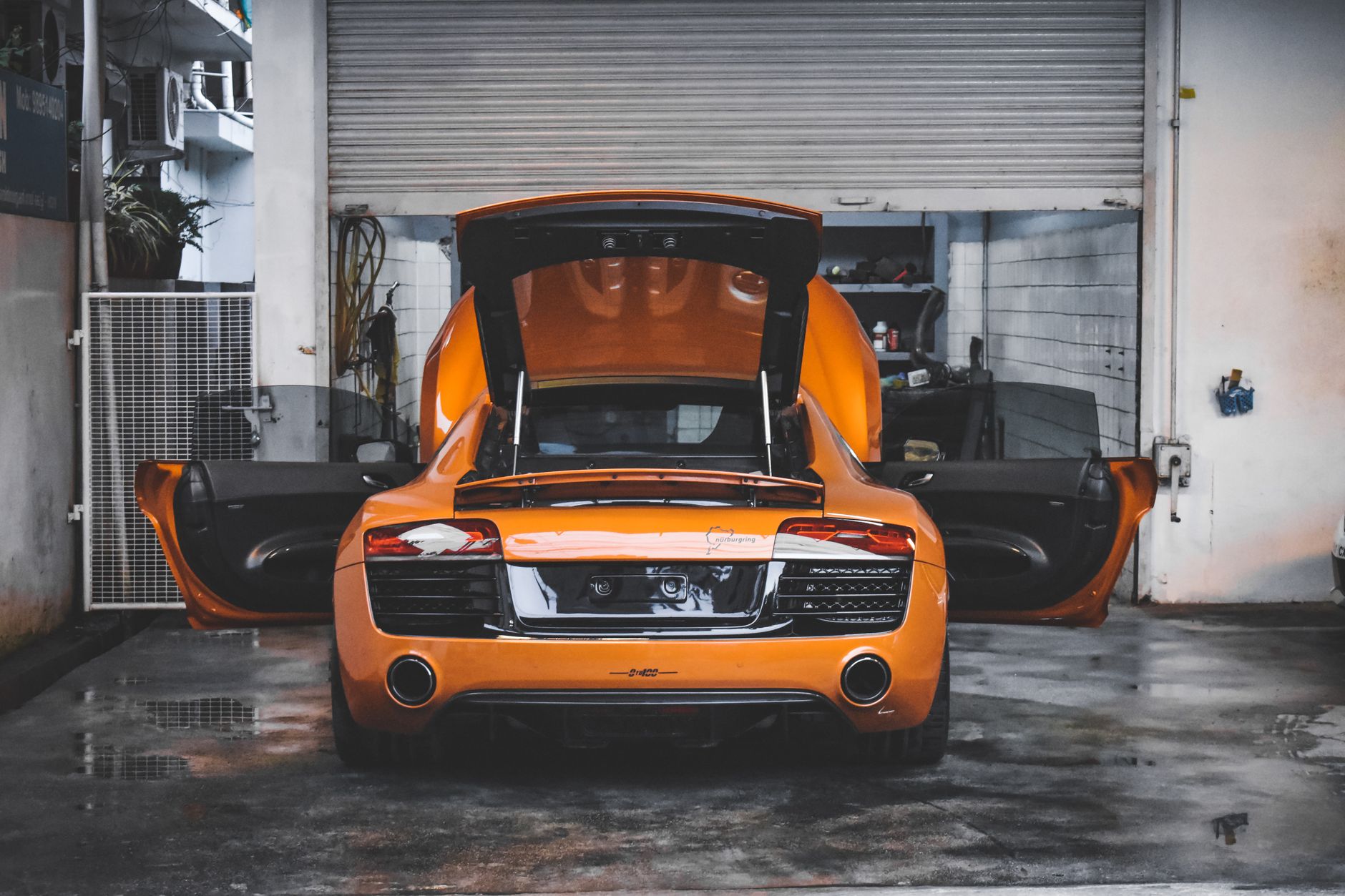 Pomarańczowy Aston Martin V8 Vantage w garażu z otwartymi drzwiami